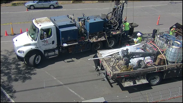 Vigil S0 Routine alert (suppressed) — workers in high-visibility vests operating drilling equipment in a commercial parking lot, May 2026